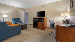 A hotel room with a sofa, a desk, a television, a microwave, and a lamp. - Comfort Inn & Suites Indianapolis Northwest - College Park (Indianapolis)