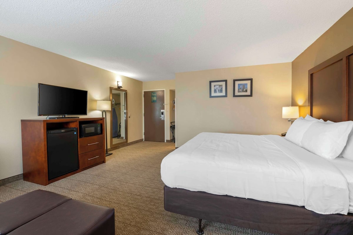 A hotel room with a bed, a TV, a desk with a microwave, and a door leading to another room.