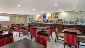 A hotel dining area with multiple tables and chairs, a kitchen counter with appliances, and a projector screen on the wall. - Comfort Inn & Suites Indianapolis Northwest - College Park (Indianapolis)