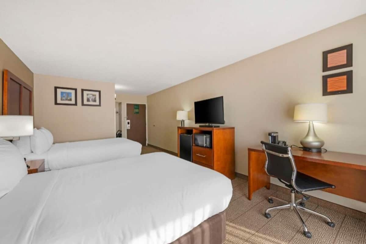 A hotel room with two beds, a desk with a chair, a television, and framed pictures on the wall.