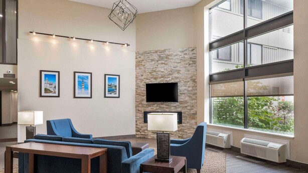 A modern hotel lobby with a stone wall, a flat-screen TV, and framed pictures on the wall. - Comfort Inn & Suites Indianapolis Northwest - College Park (Indianapolis)