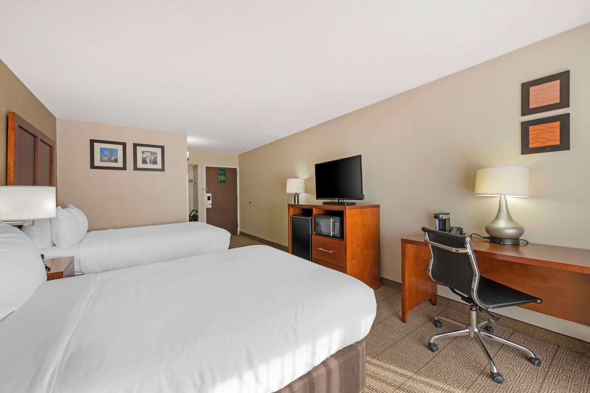 A hotel room with two beds, a desk, a chair, a television, and a lamp.