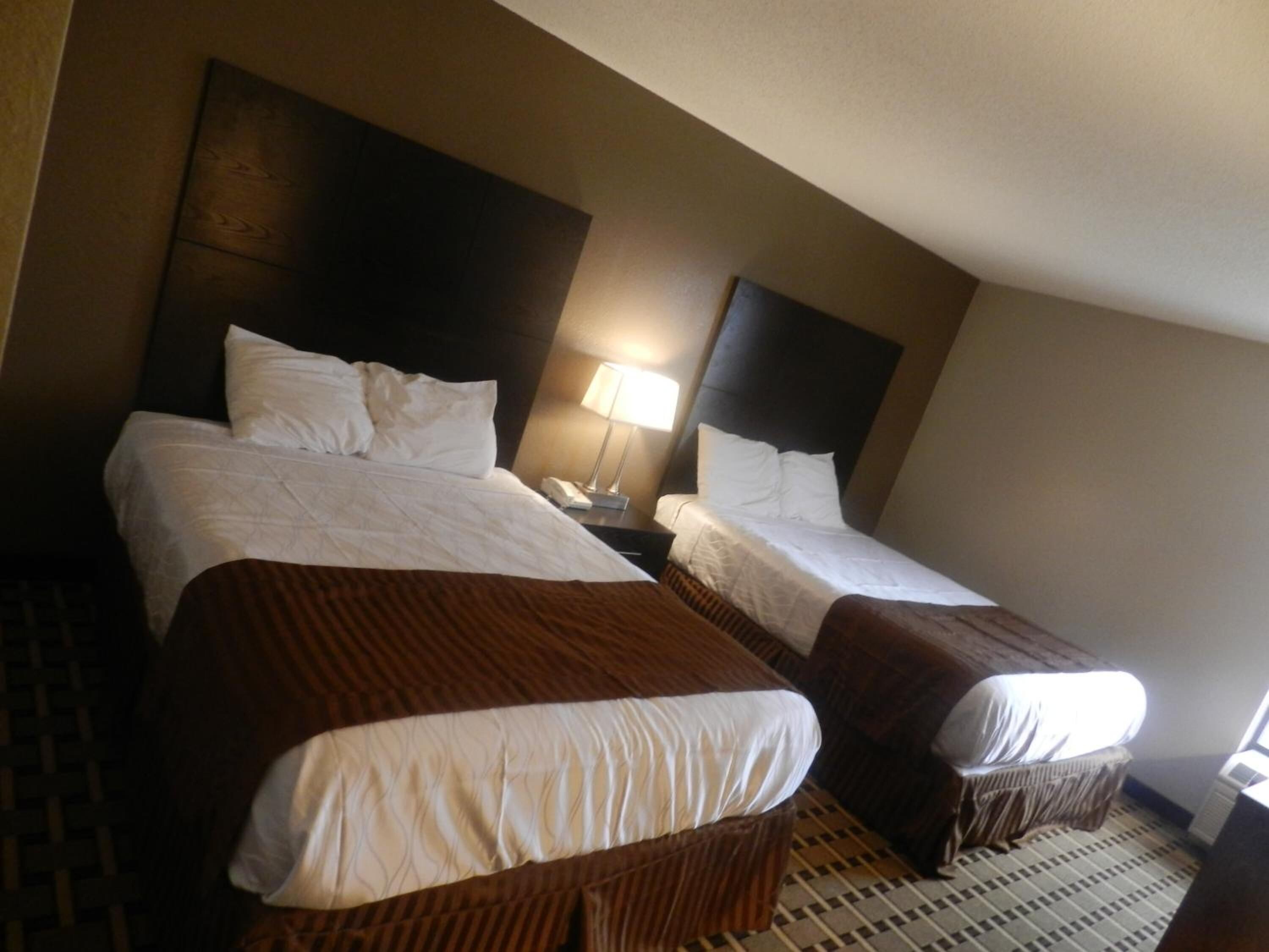 A hotel room with two beds, a nightstand with a lamp, and a patterned floor.