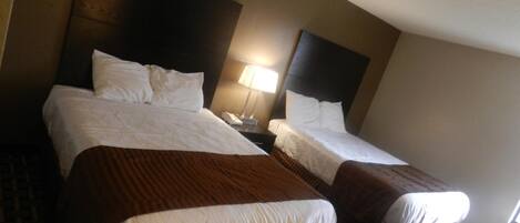 A hotel room with two beds, a nightstand with a lamp, and a patterned floor.