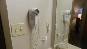 Un bagno d'hotel con un asciugacapelli fissato alla parete, uno specchio e un distributore di asciugamani.