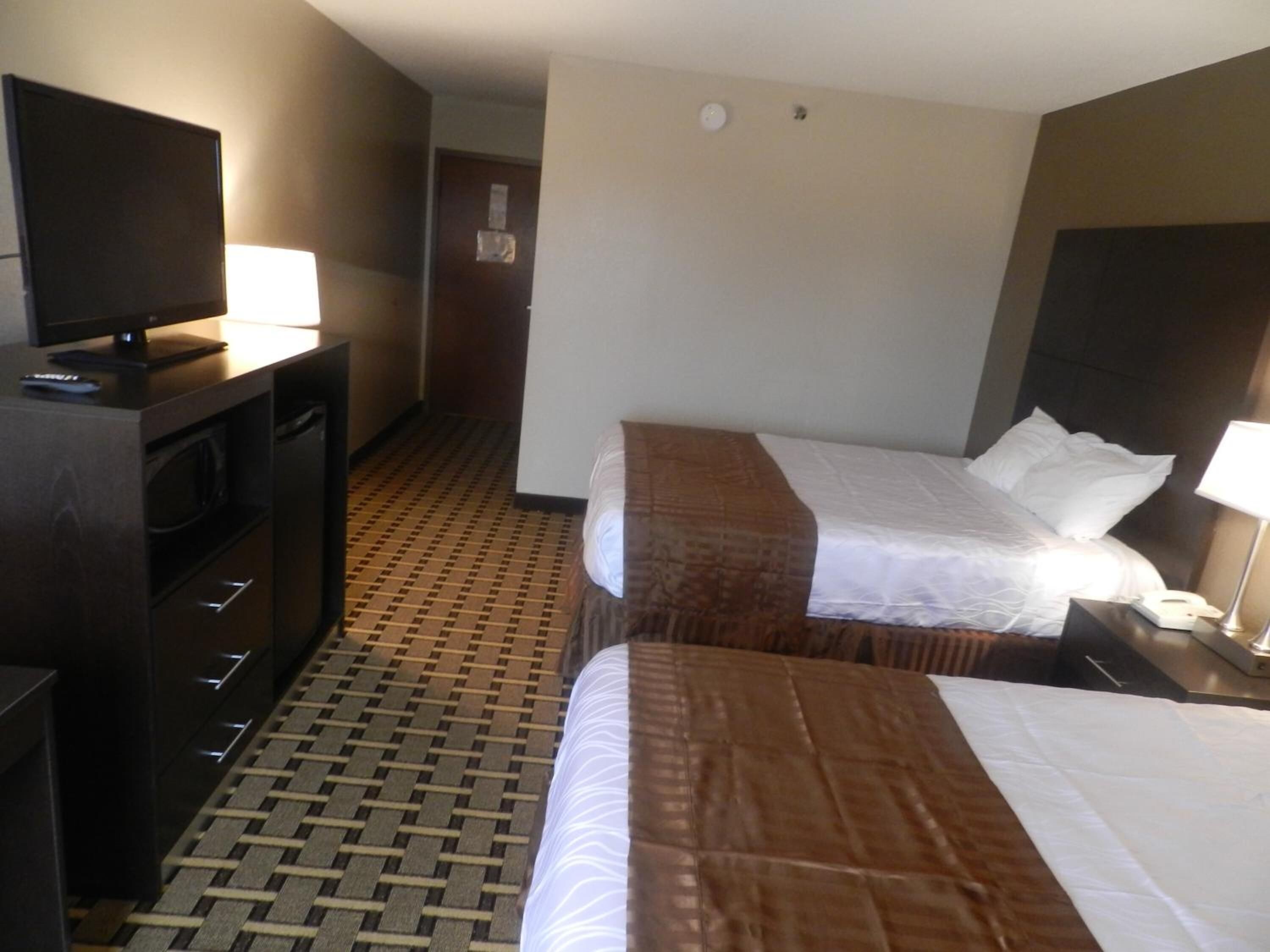 A hotel room with two beds, a TV, a desk with a lamp, and a microwave.