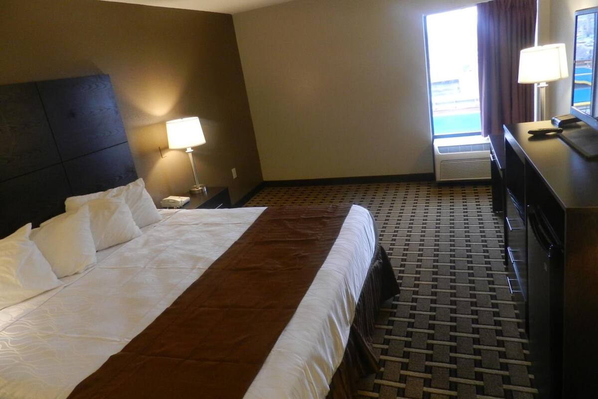 Una habitación de hotel con una cama grande, un escritorio con lámpara, vistas al exterior a través de una ventana y una alfombra estampada.