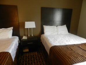 Una habitación de hotel con dos camas, una mesita de noche con lámpara y un tapete tejido en el suelo.