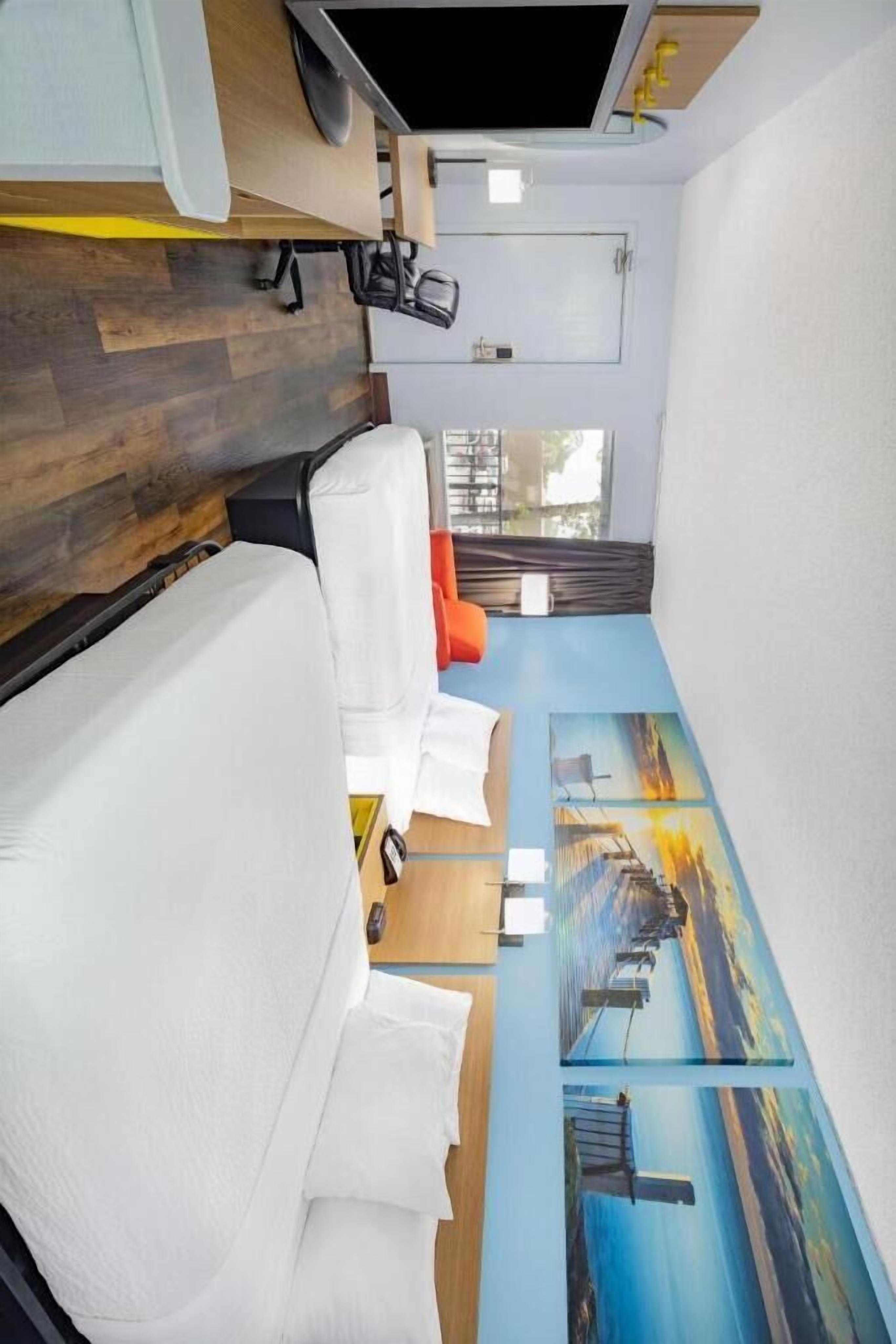 Una habitación compacta con una cama, un pequeño rincón de descanso y un mural en la pared.