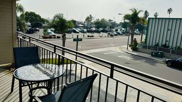 A balcony with a tiled table and chairs, overlooking a parking lot with cars and palm trees.