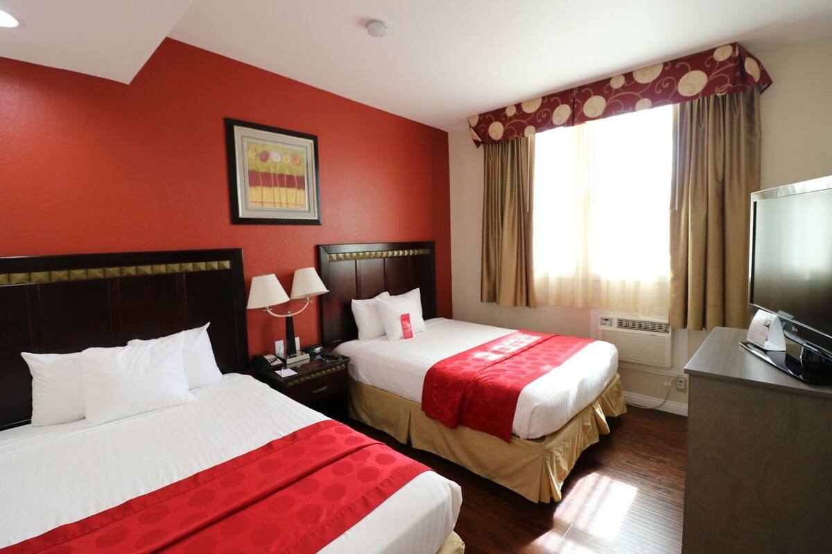 A hotel room with two beds, a television, a desk, and a window with curtains.