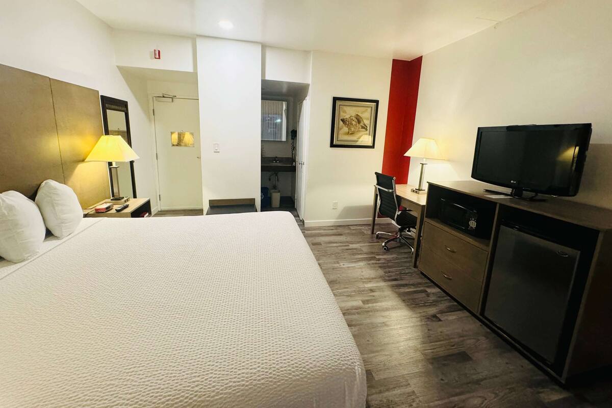 A hotel room with a bed, desk, television, and a kitchenette.