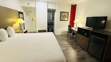 Quarto de hotel com cama, escrivaninha, televisão e cozinha compacta.