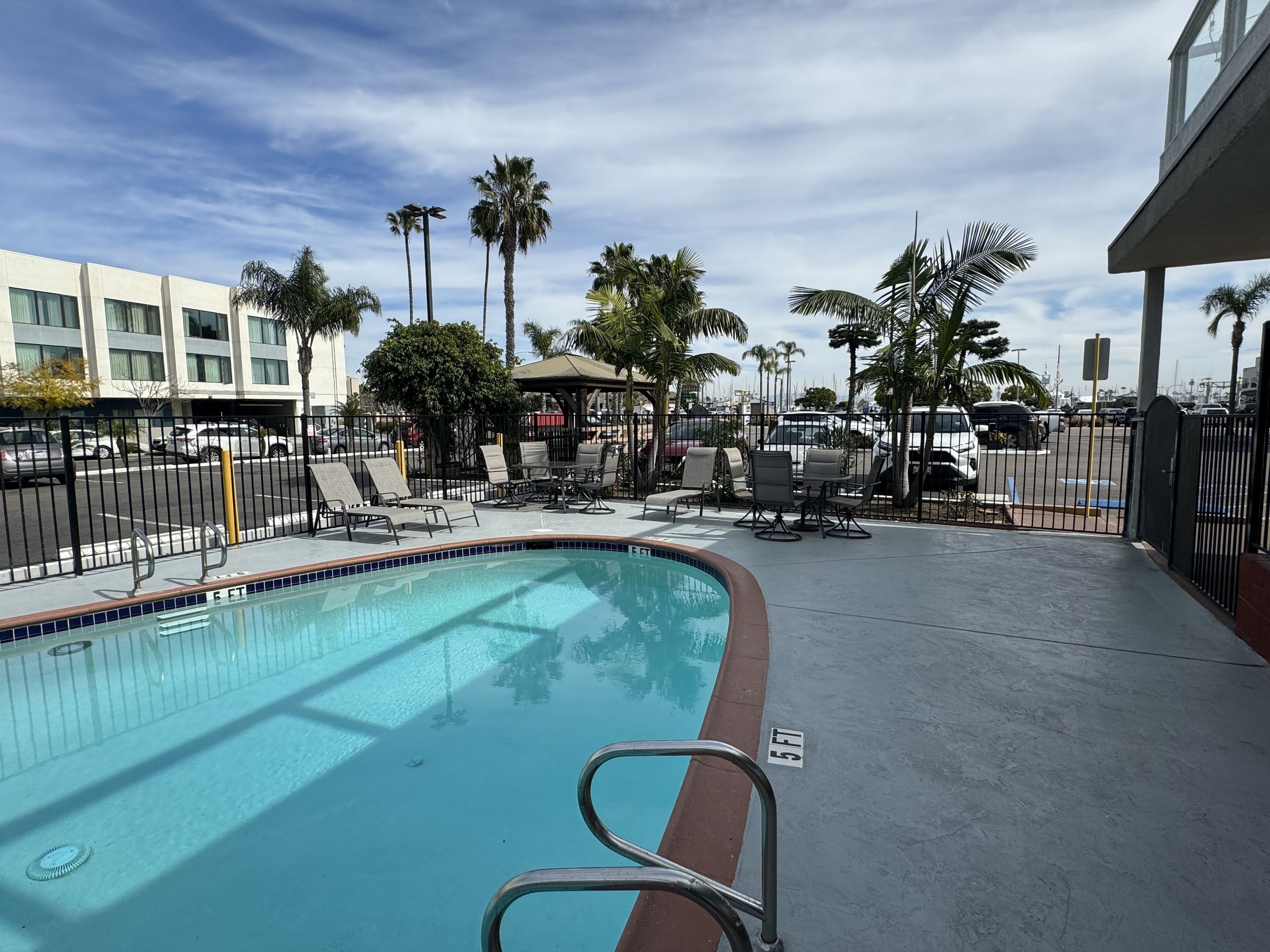 A swimming pool with lounge chairs and umbrellas, surrounded by palm trees and a building in the background.