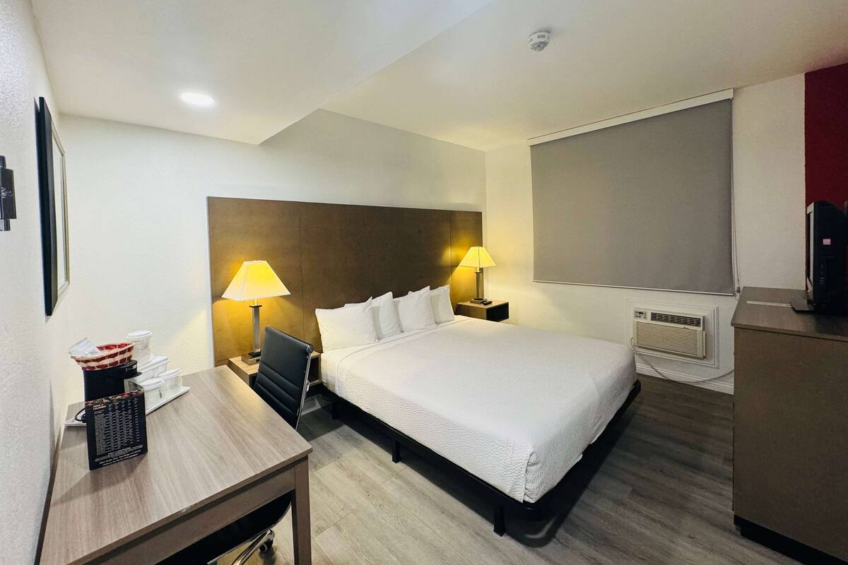 A hotel room with a large bed, two bedside lamps, a desk with a coffee maker, and a TV.