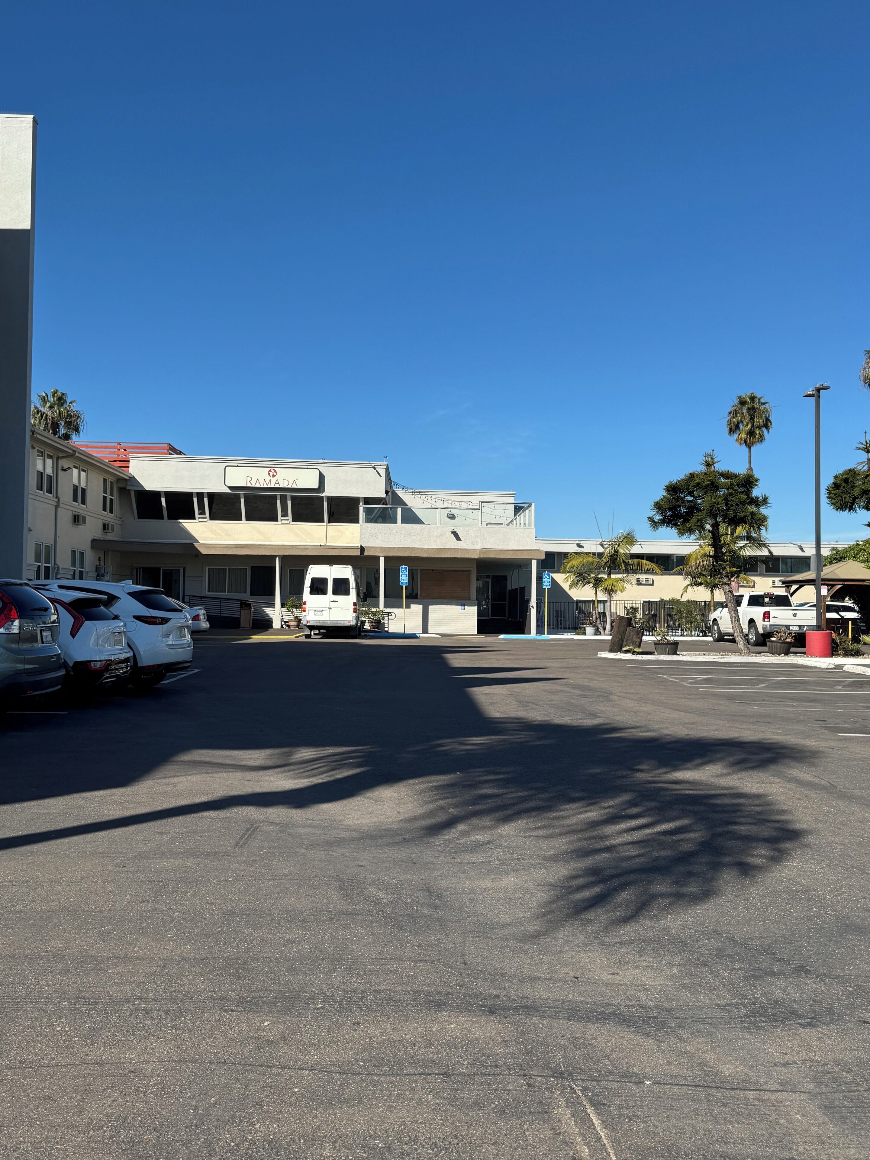 A parking lot with several cars, a white van, and a building labeled "RAMADIA".
