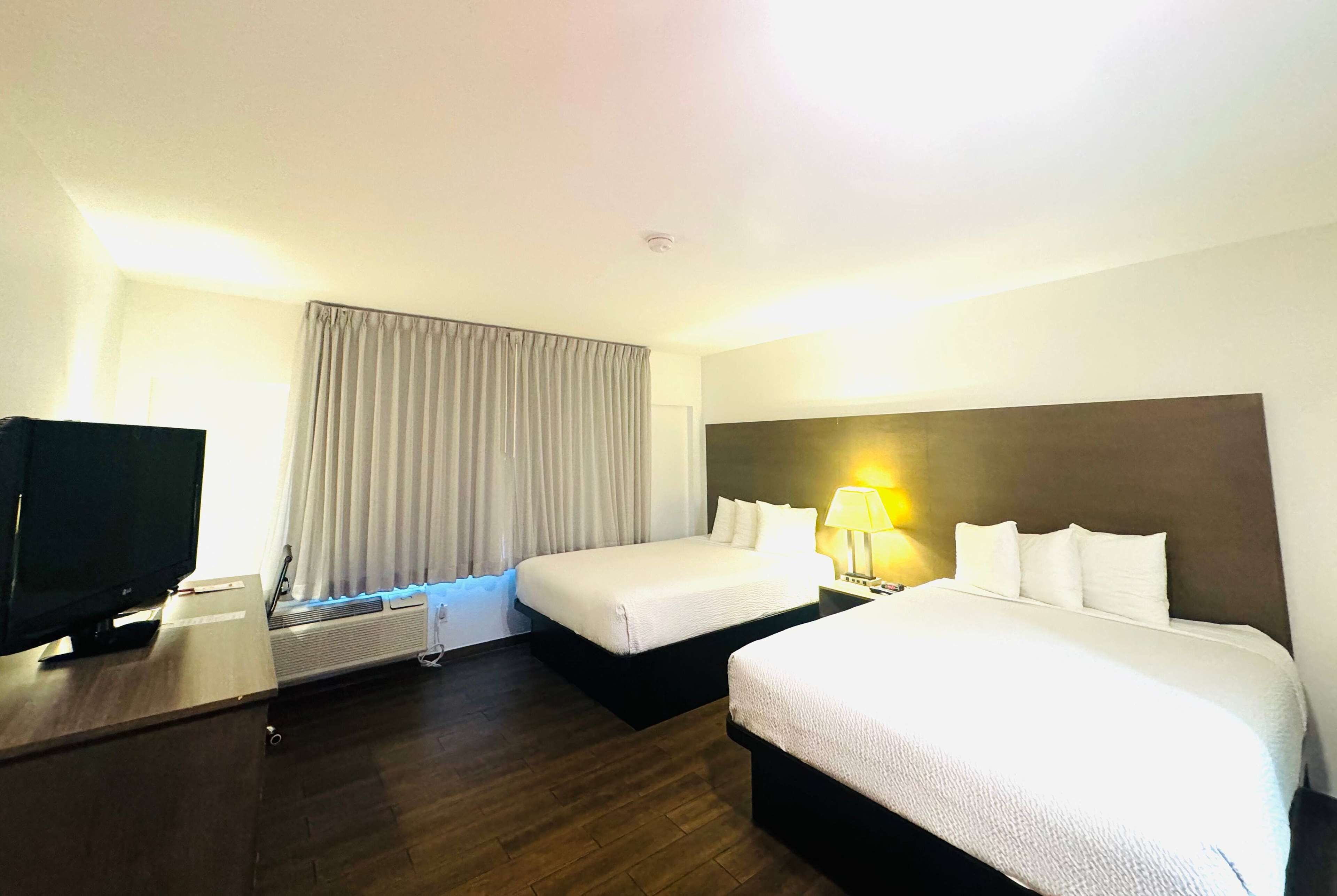 A hotel room with two beds, a television, a lamp, and a window with curtains.