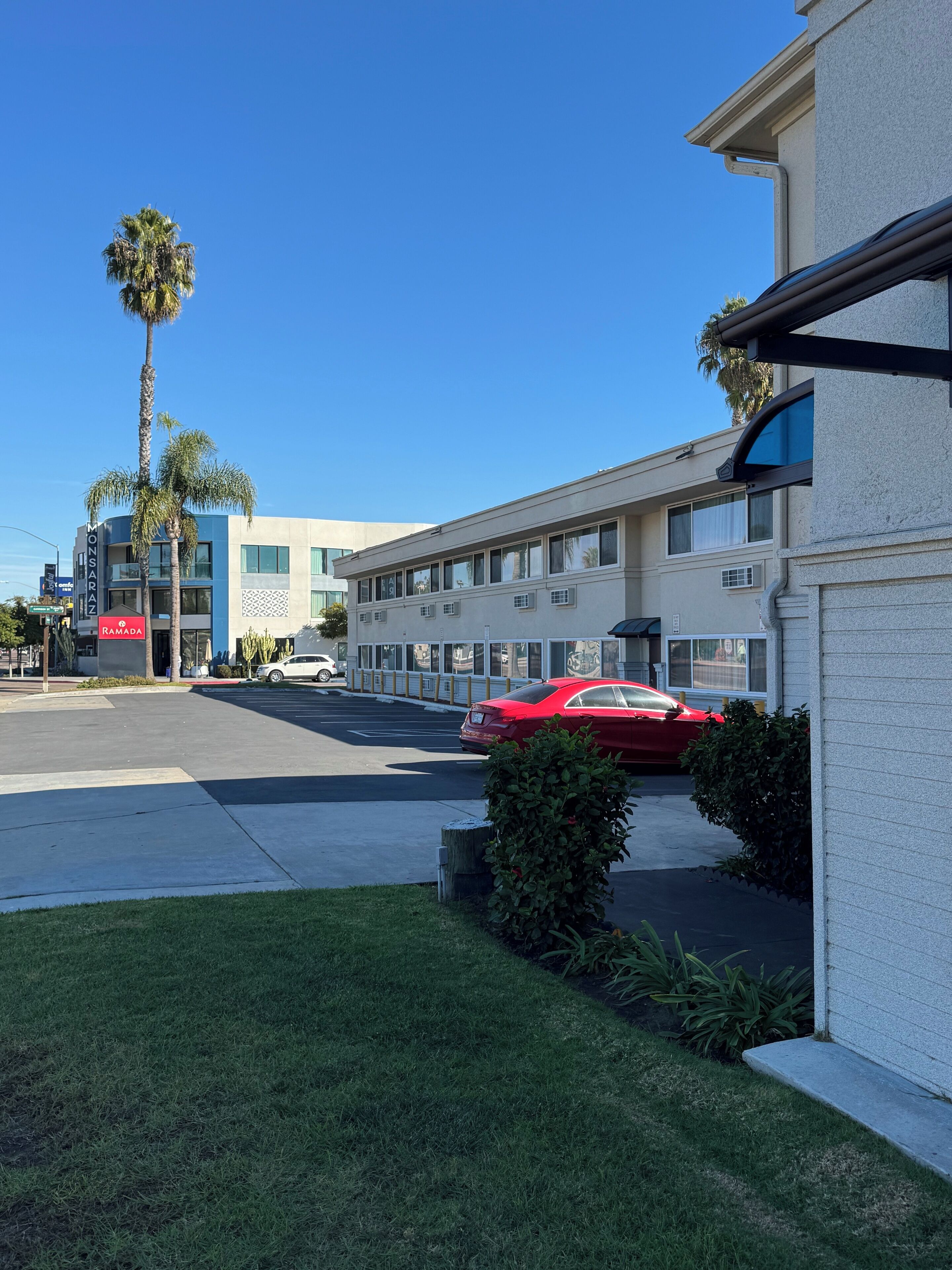 Un hôtel moderne doté d’un parking, avec une voiture rouge garée devant et un palmier.