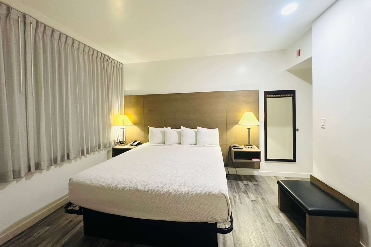A hotel room with a large bed, two bedside tables with lamps, a wardrobe, and a bench.