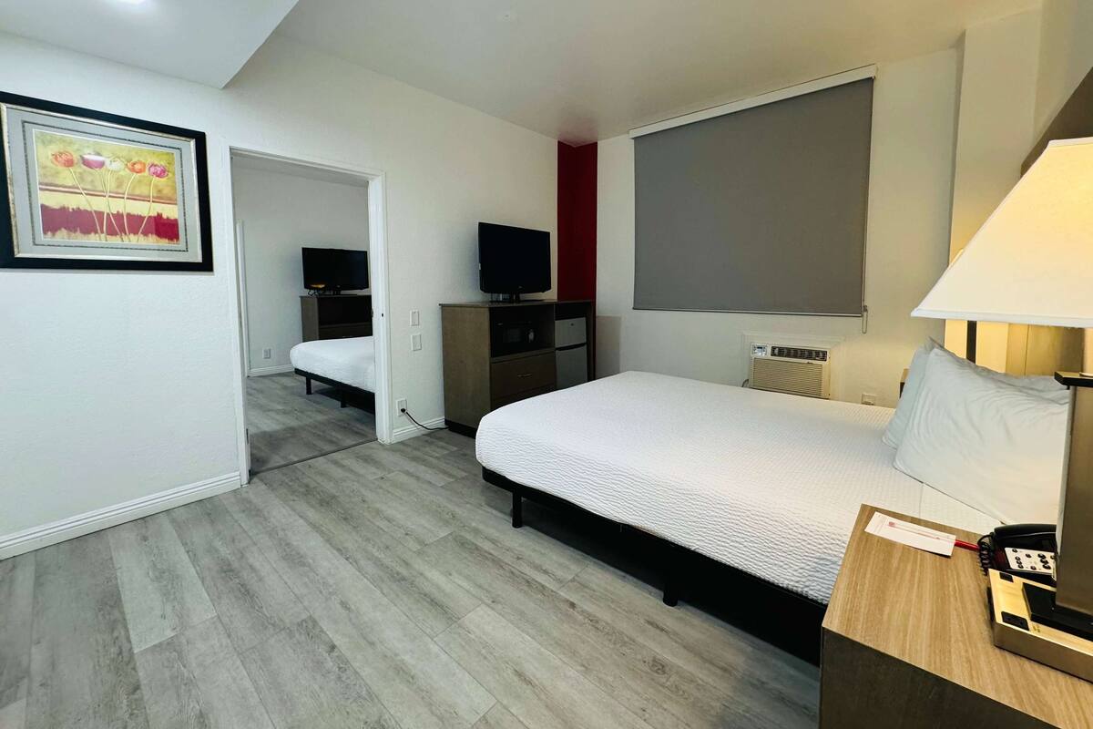A hotel room with a bed, a desk with a lamp, a TV, and a painting on the wall.