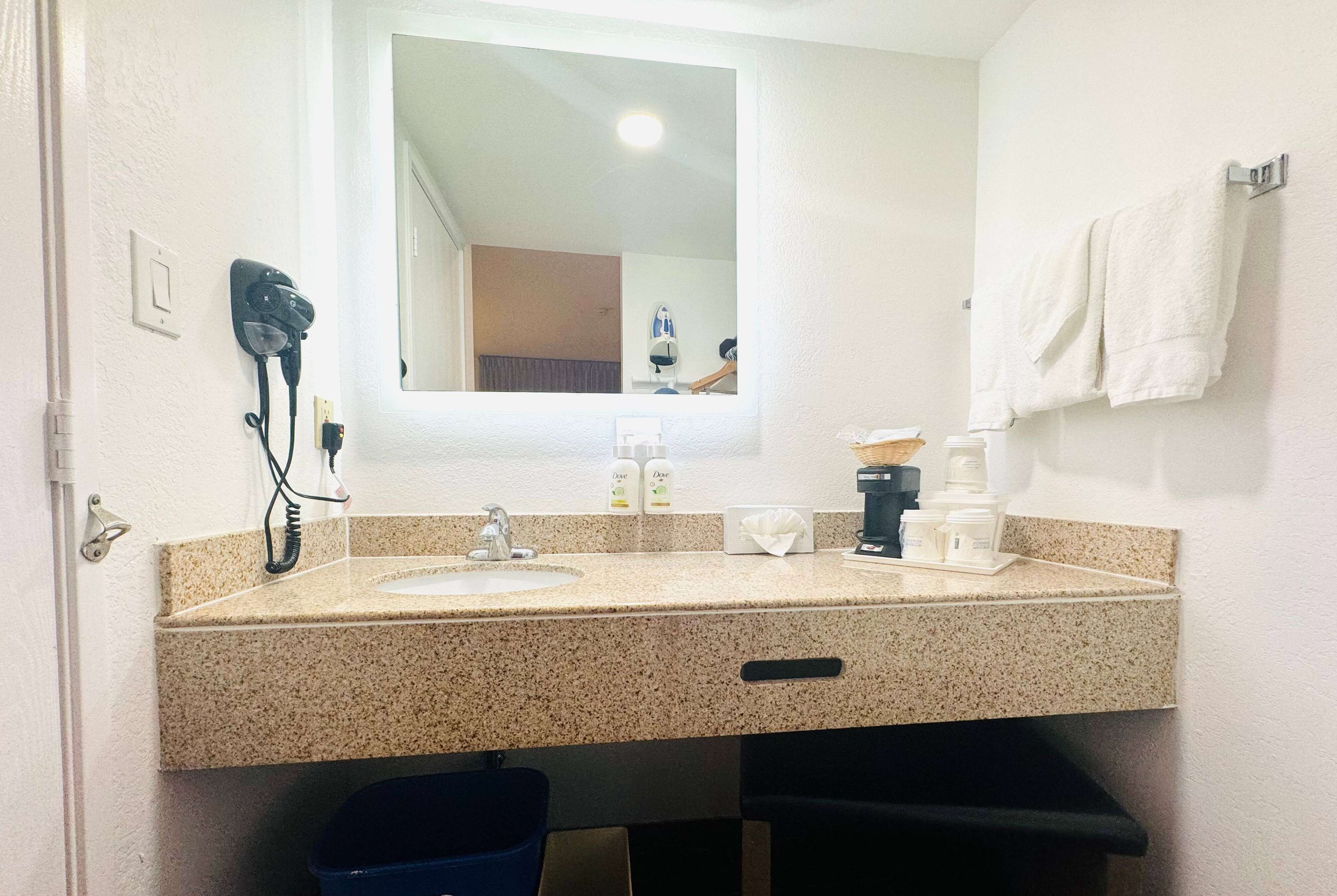 A bathroom with a sink, mirror, hairdryer, and towels.