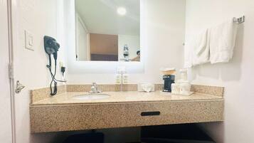 A bathroom with a sink, mirror, hairdryer, and towels.