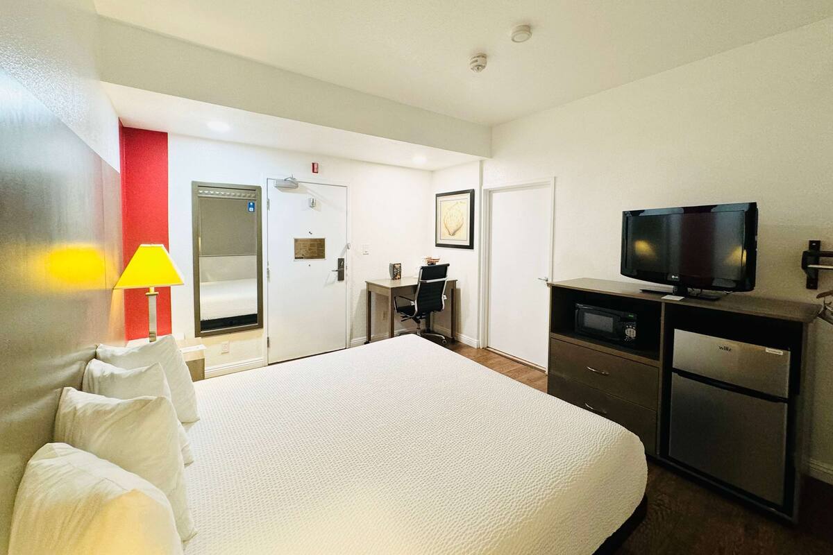 A hotel room with a large bed, a desk with a chair, a television, a microwave, and a refrigerator.