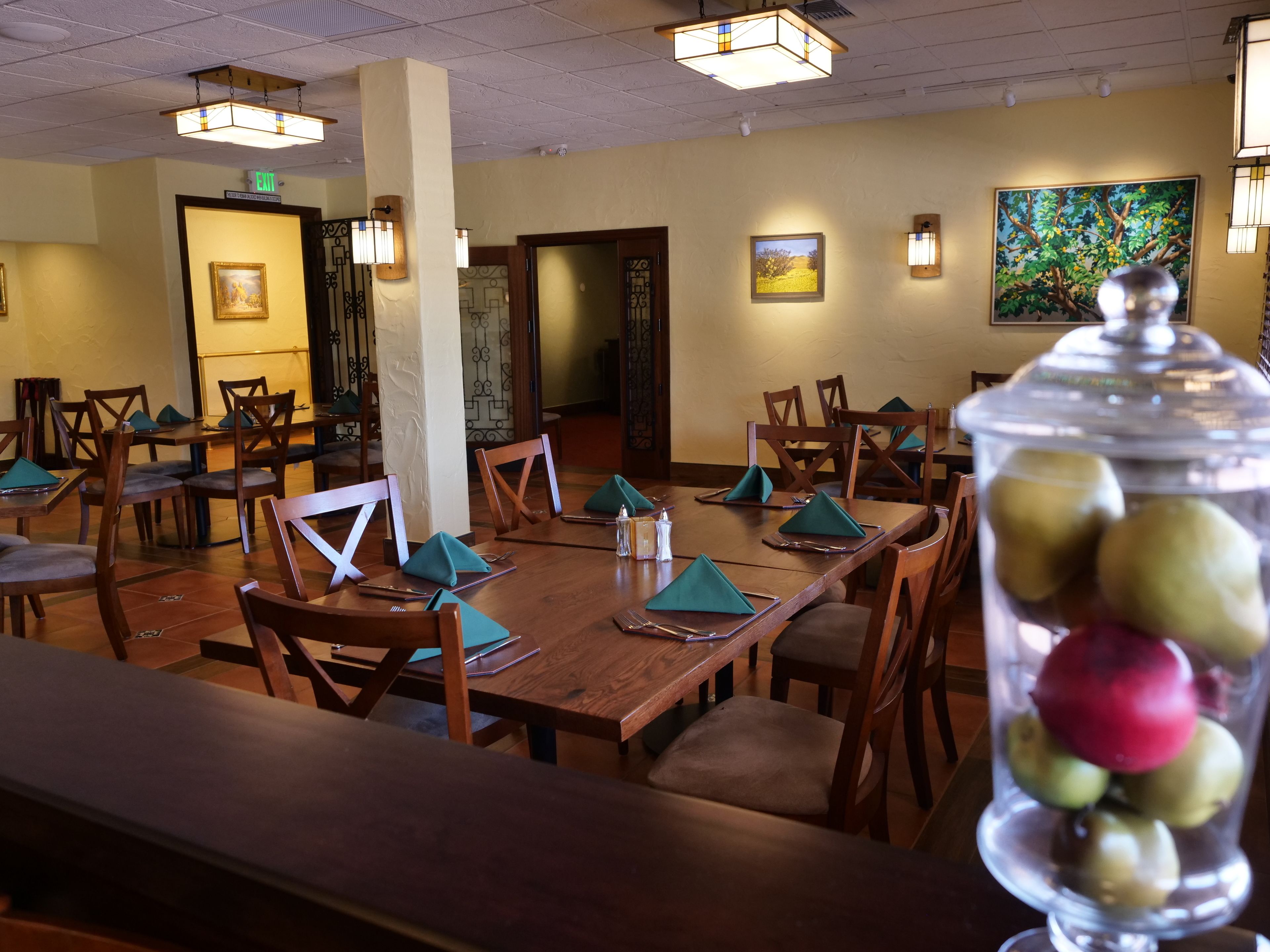 Un restaurant avec des tables et des chaises en bois, une vitrine où sont exposés des fruits et des tableaux encadrés accrochés aux murs.