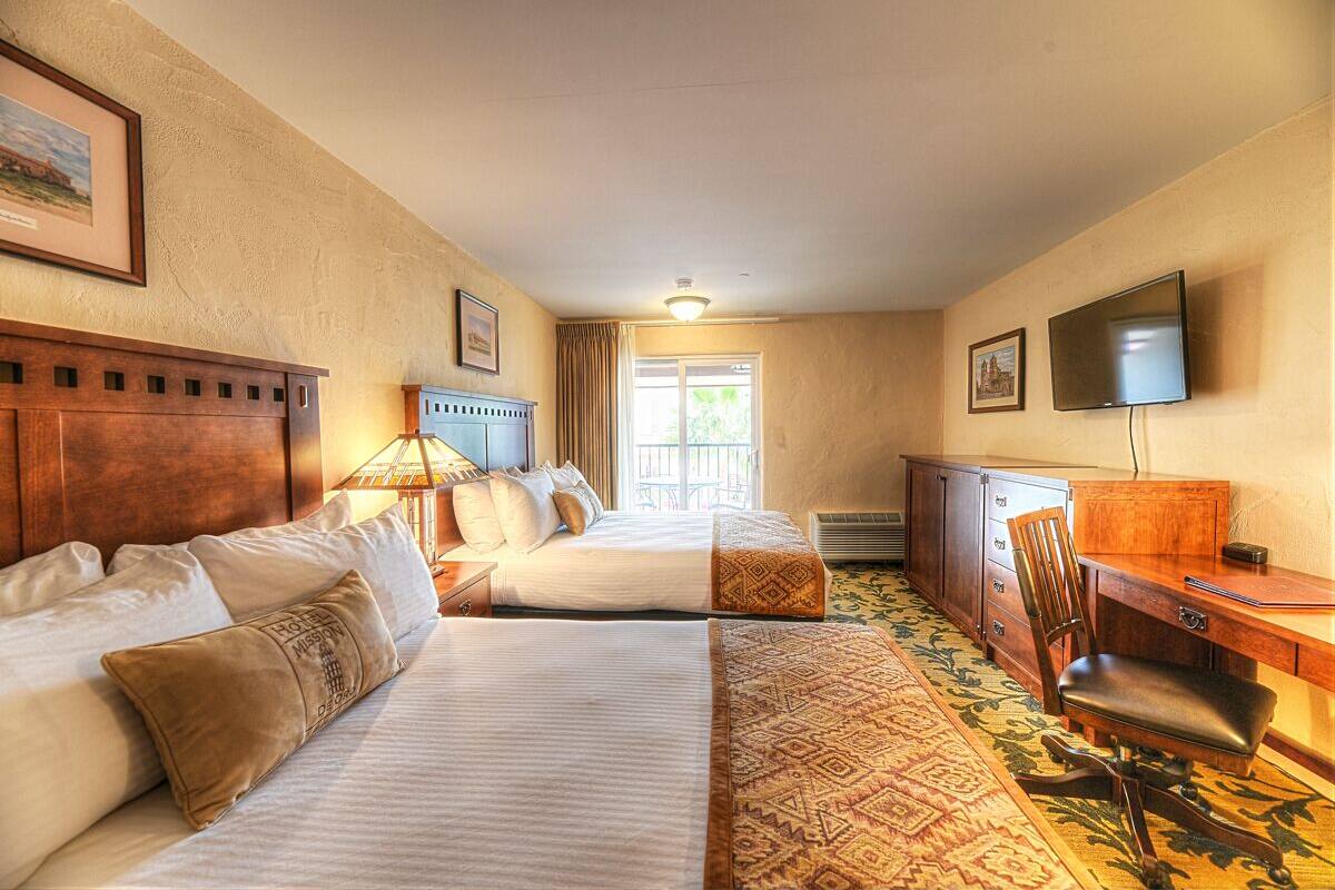 A hotel room with two beds, a desk, a chair, a television, and a window with curtains.