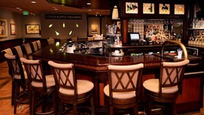 A bar area with a long wooden bar, multiple stools, and a well-stocked bar counter. - Hotel Mission de Oro (Gustine)