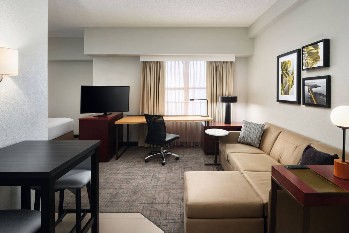 A hotel room with a bed, a desk with a chair, a television, a sofa, and a small table.