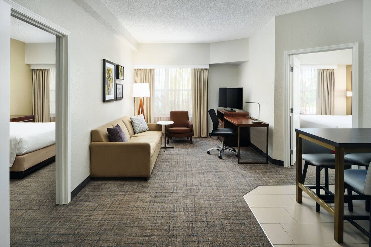 A hotel room with a bed, a sofa, a desk, a TV, and a chair.