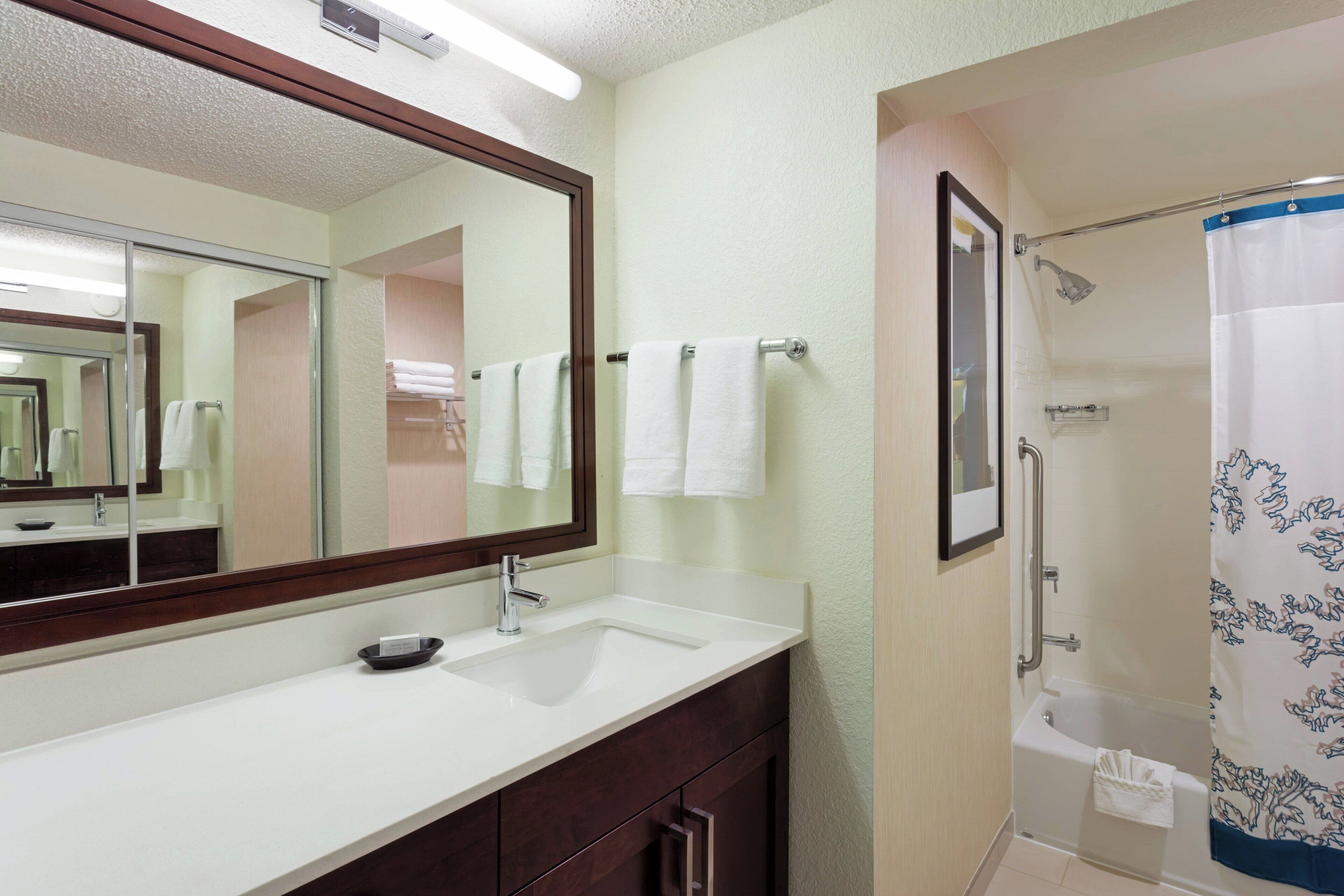 A bathroom with a white sink, a mirror, a shower with a blue floral curtain, and a towel rack with white towels.