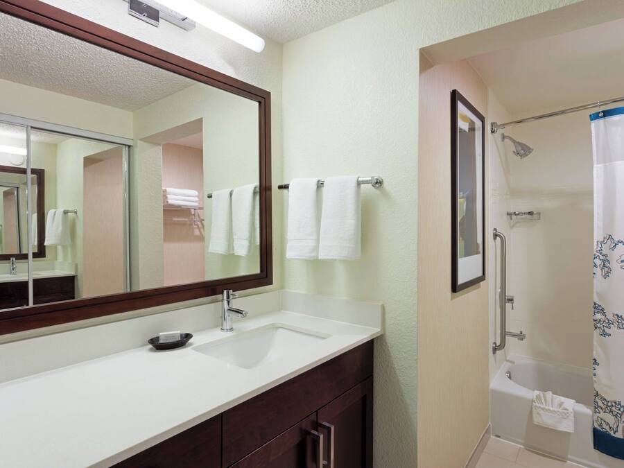 A bathroom with a white sink, a mirror, a shower with a blue floral curtain, and a towel rack with white towels.