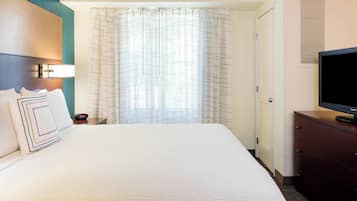 A hotel room with a large bed, a television on a dresser, a nightstand, and a window with curtains.