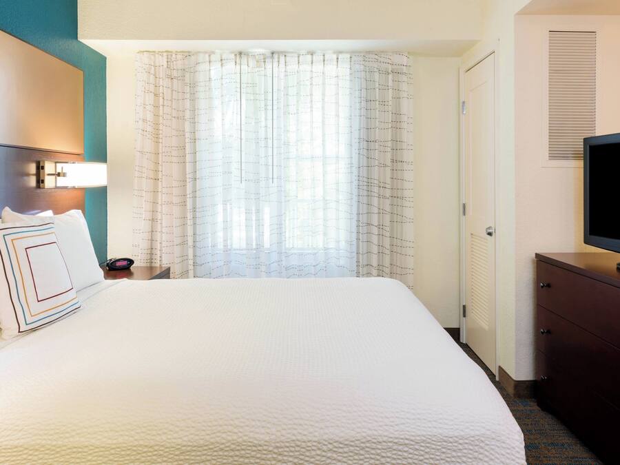 A hotel room with a large bed, a television on a dresser, a nightstand, and a window with curtains.