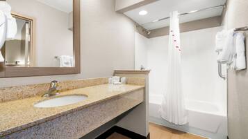Un baño con lavamanos de encimera de granito, espejo, ducha con cortina y bañera.