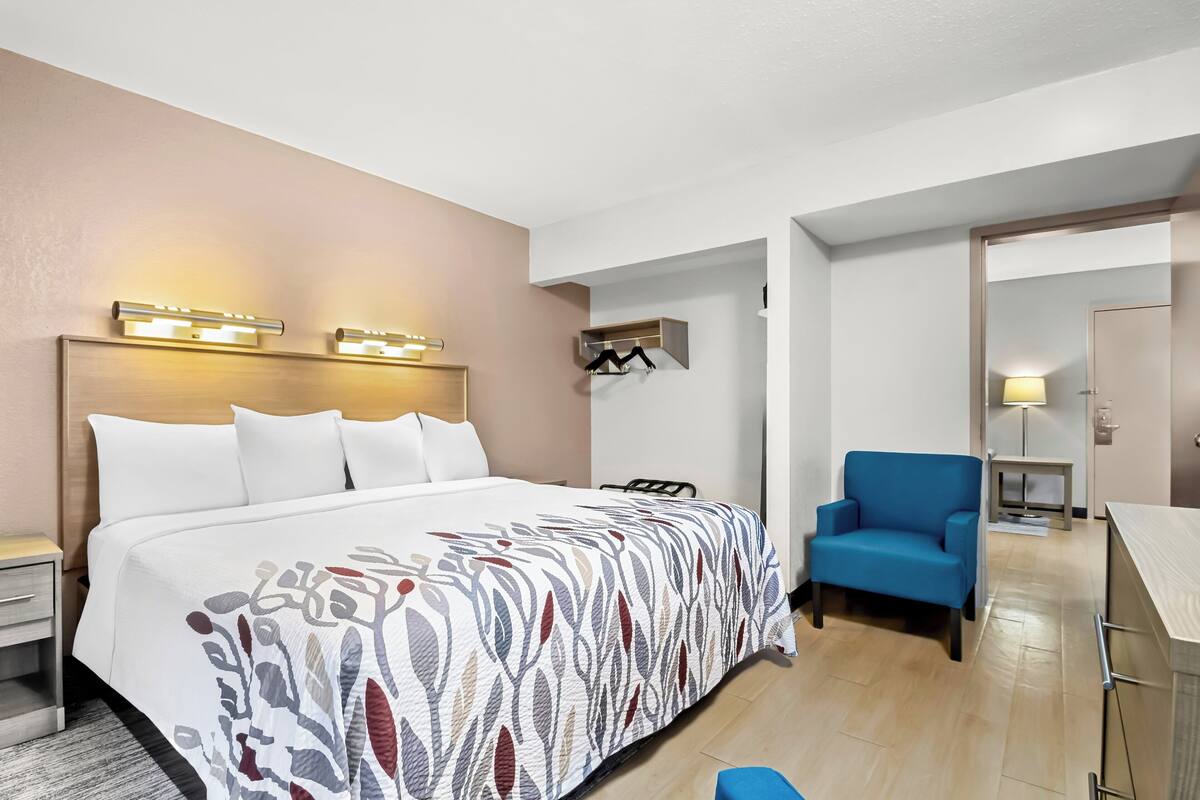 Una habitación de hotel con cama, mesita de noche, lámpara, silla y escritorio con otra silla.