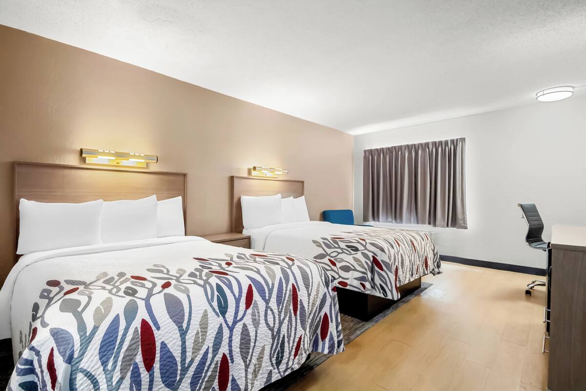 A hotel room with two beds, a desk, and a chair.