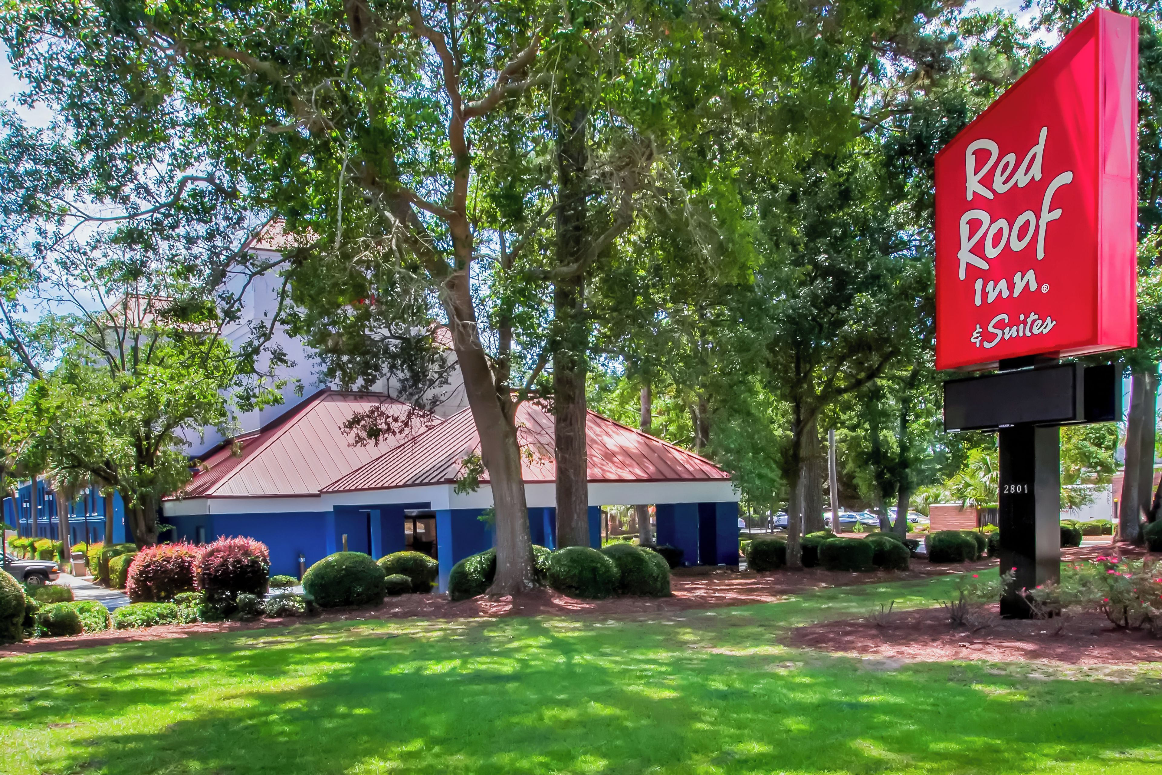 A Red Roof Inn & Suites with a red roof, surrounded by lush greenery and a well-maintained lawn.