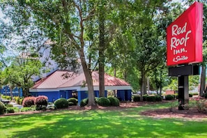 Un hôtel Red Roof Inn & Suites, reconnaissable à son toit rouge, entouré d’une végétation luxuriante et d’une pelouse bien entretenue.