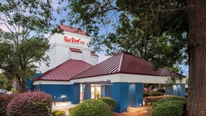 Un hôtel Red Roof Inn avec un toit rouge et des murs blancs, entouré d’arbres et d’arbustes.
