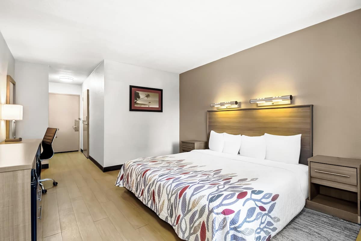 Habitación de hotel con una cama grande, un escritorio con silla, una mesita de noche y una lámpara de pared.