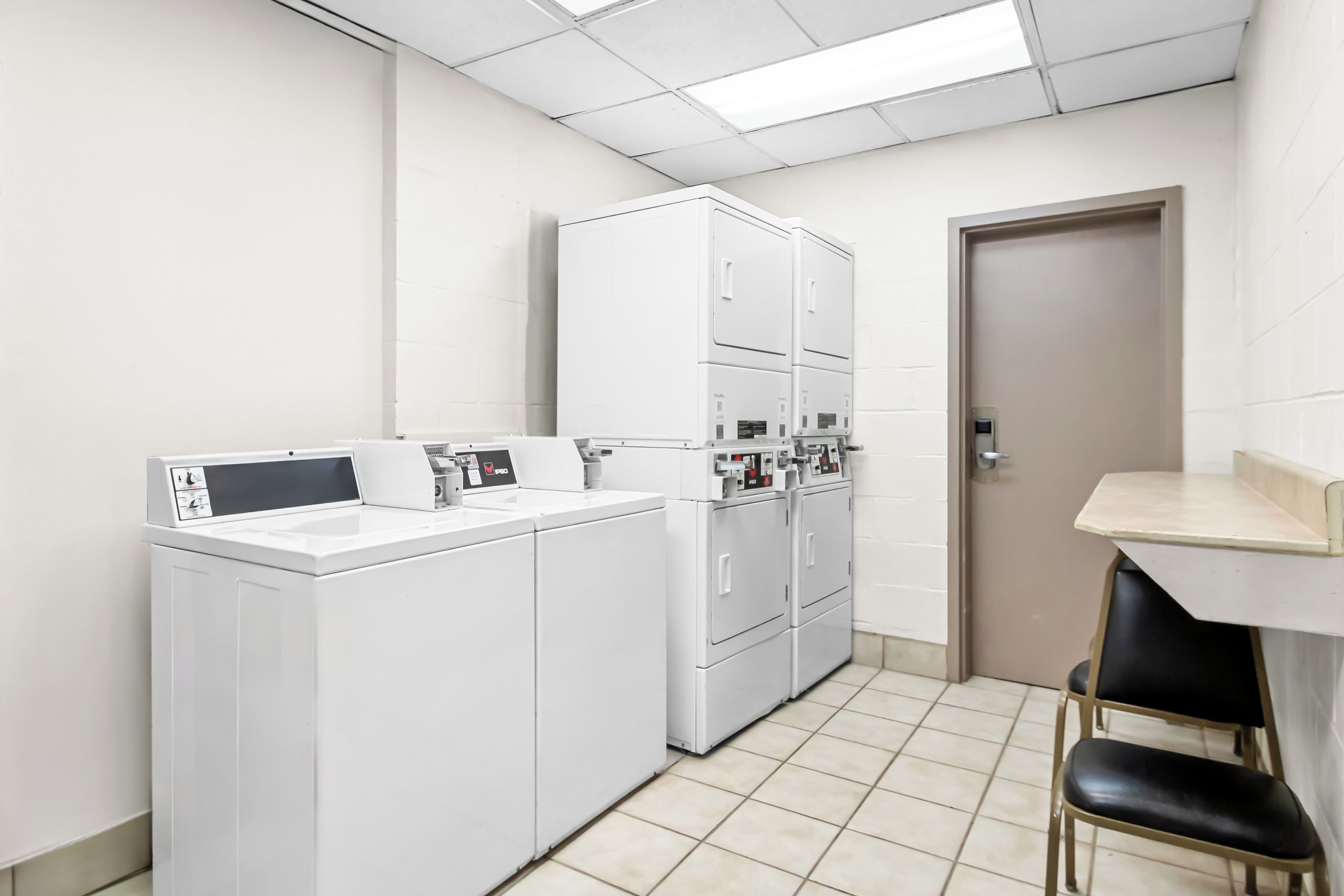 A laundry room with a washing machine, dryers, and a small table with chairs.