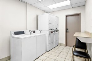 Une buanderie équipée d’un lave-linge, de plusieurs sèche-linge et d’une petite table avec des chaises.