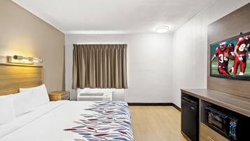 A hotel room with a bed, a flat-screen TV, a desk with a microwave, and a window with curtains.