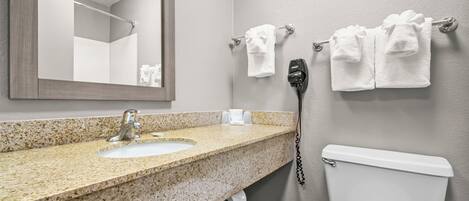 A bathroom with a granite countertop sink, a mirror, a towel rack with towels, a hairdryer, and a toilet.