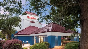 Un hôtel Red Roof Inn avec un toit rouge et des murs blancs, entouré d’arbres et d’arbustes.