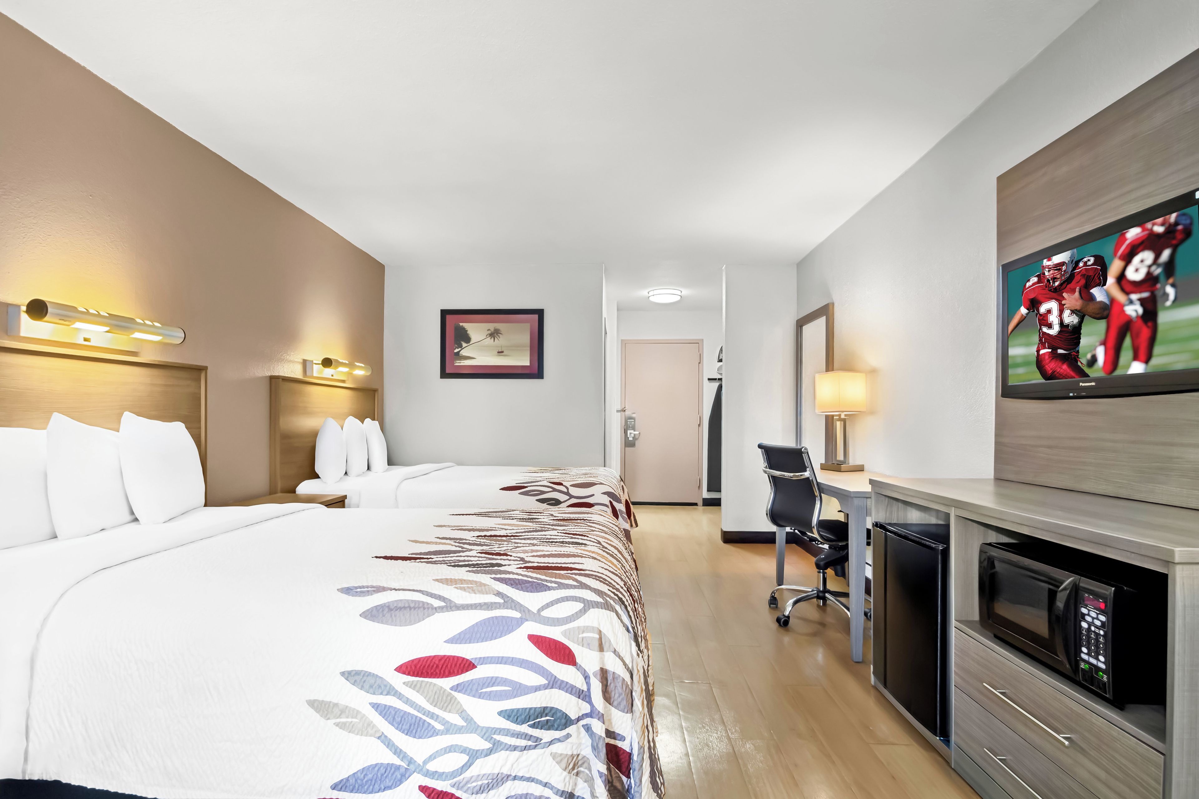 A hotel room with a bed, a desk, a television, and a door.