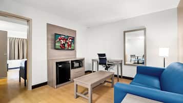 Quarto de hotel com televisão de tela plana na parede, pequena geladeira, micro-ondas, escrivaninha com cadeira e sofá azul.